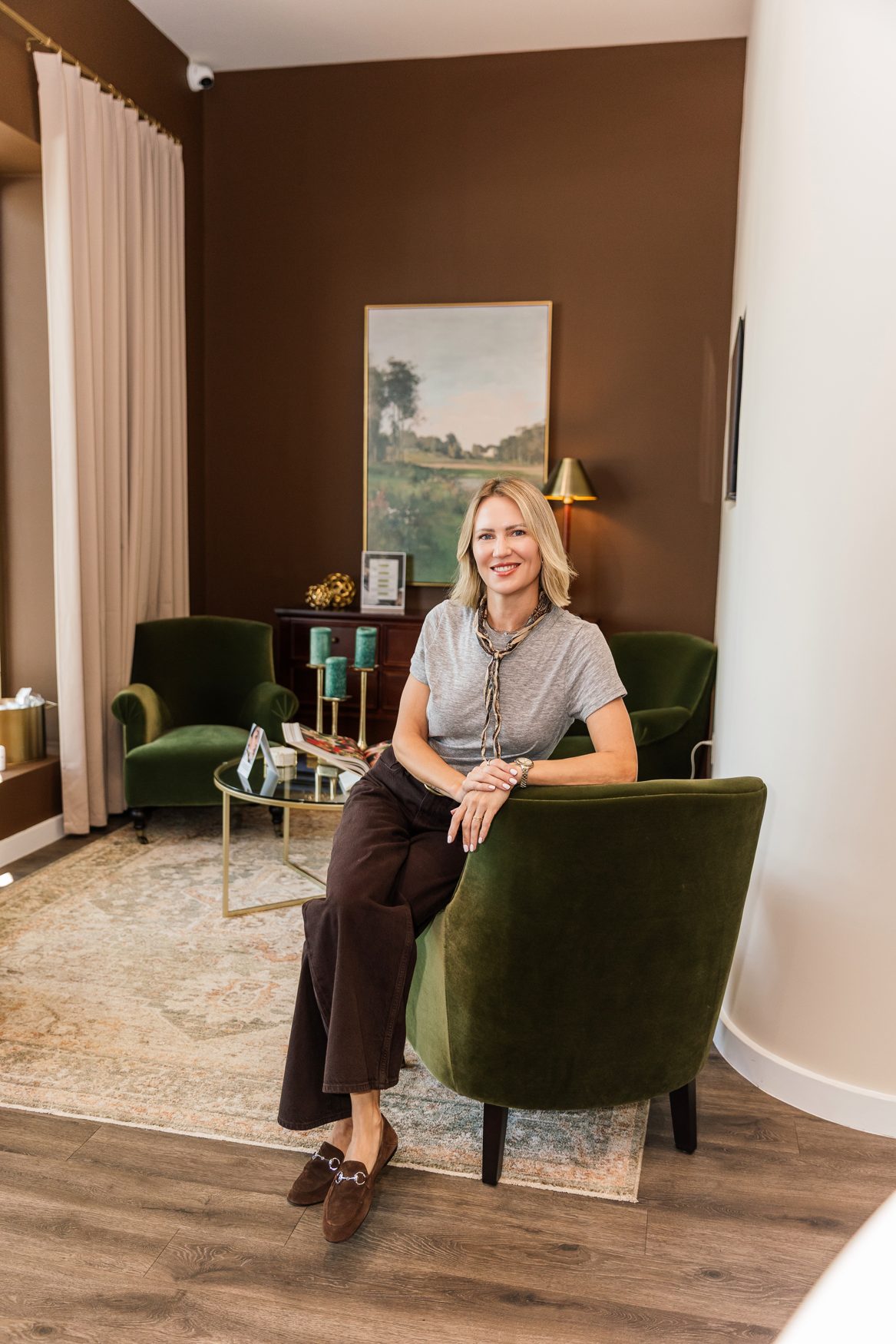 Lindsey Strelecki, BSN, RN seated in a green velvet armchair in the consultation lounge at Manor Aesthetics & Wellness in Fort Worth